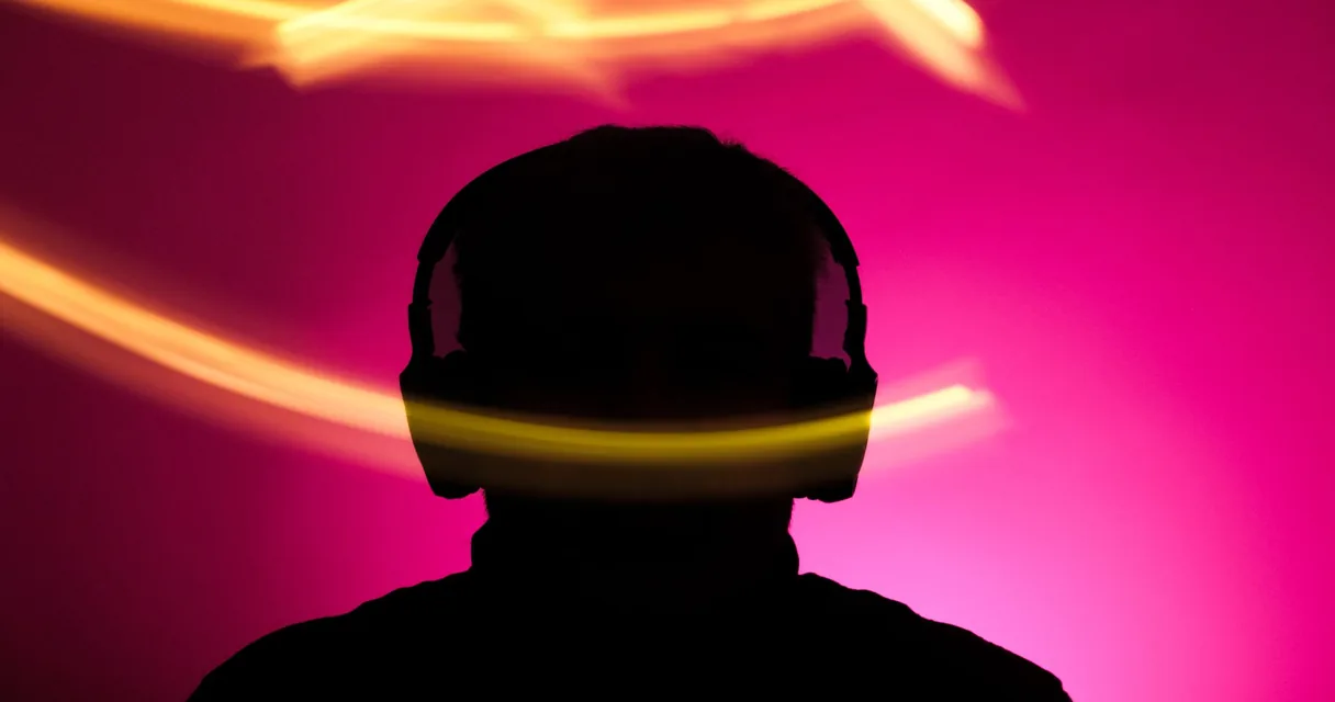 Silhueta de pessoa com fones de ouvido diante de fundo rosa e luzes amarelas, ilustrando o idioma do áudio no IPTV